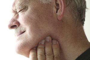 Older man touches a sore area of his jaw.